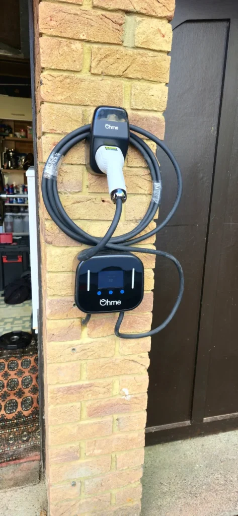 Ohme Home Pro EV charger with a coiled tethered cable and connector holder beside a garage in Milton Keynes