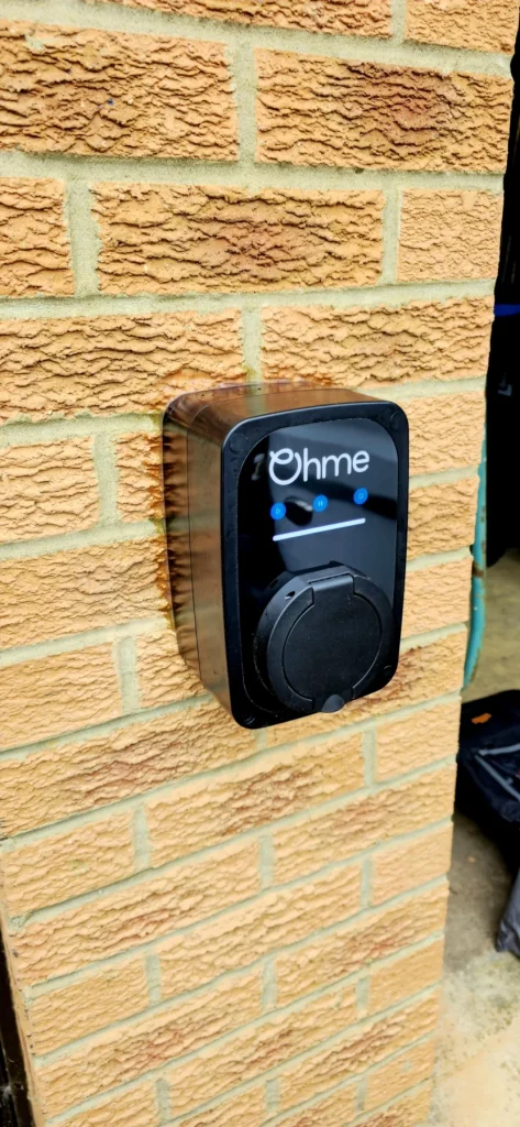 Black untethered Ohme EV charger mounted on an external brick wall in Milton Keynes